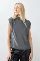 Blusa plateada de lurex con cuello alto y tablas en los hombros. Sin mangas.