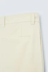 Pantalón chino color beige, corte recto, con bolsillos laterales y traseros. Cierre frontal con cremallera y botón.