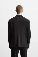 Blazer slim fit negra confeccionada en tejido con viscosa. Cuello con solapas de muesca, manga larga con puño con detalle de botones, bolsillo de vivo en pecho y de solapa en cadera, bolsillo interior, bajo con aberturas en espalda y cierre frontal con botones.