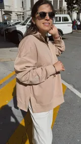 Buzo color beige con cuello alto y cierre parcial, de corte holgado y mangas largas con puños ajustados.
