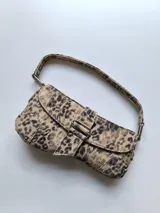 Cartera tipo baguette con estampado animal print, cierre superior con solapa y hebilla decorativa.