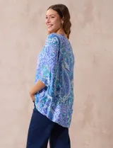 Blusa de gasa estampada con motivos paisley en tonos azules, marca Ruby Rd. Tiene cuello redondo con escote en V y aplique metálico. Presenta una sobre capa delantera y terminación asimétrica. Las mangas son 3/4 y amplias.