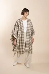 Ruana marrón con diseño a cuadros blancos, terminación envivada y flecos cortos.