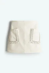 Minifalda color crema de tejido revestido con bolsillos grandes parche adornados con ojales de metal y pespuntes decorativos sobredimensionados. Modelo de tiro alto con cierre oculto y cierre de corchete atrás. Forrada.