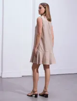 Vestido corto blanco sin mangas, con cuello camisero, abotonadura frontal parcial y ruedo con volantes.