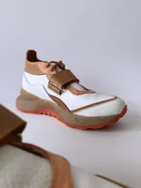 Zapatillas deportivas blancas con detalles en cuero color salmón y suela gruesa con detalles en naranja.