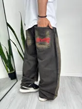 Pantalón baggy de denim color gris oscuro con efecto gastado. Tiene bolsillos delanteros y traseros, y un bordado rojo con la palabra "Rockstar" en el bolsillo trasero derecho.