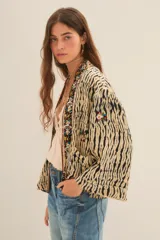 Kimono de manga ancha, estilo japonés, con estampado que imita piel de cebra en tonos beige y negro. El borde está decorado con apliques de mostacillas y bordados florales en tonos rojizos, verdes y dorados.