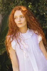 Blusa de lino color blanco, sin mangas, con cuello fruncido y volados de encaje en las sisas. Presenta pinzas frontales y un diseño de calce holgado de estilo romántico.