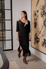 Vestido negro de noche con mangas 3/4, cuello en V con detalles de cuero entrelazado, terminación en flecos y tajos laterales.