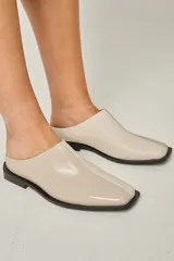 Zuecos color beige confeccionados en cuero vacuno, con punta cuadrada y suela plana color negro.