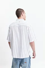 Camisa de manga corta con corte oversize, a rayas verticales blancas y grises, con cuello clásico y cierre frontal con botones. Confeccionada en algodón.