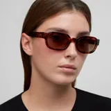 Lentes de sol con montura gruesa de acetato color carey (tortoise) y forma ligeramente cuadrada/ovalada. Los lentes son polarizados de color marrón.