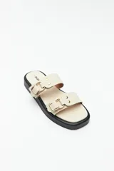 Sandalias bajas color beige con plataforma de 2,5 cm y tiras de cuero sintético con hebillas metálicas doradas.