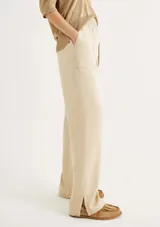 Pantalón negro de tiro alto con cintura elástica fruncida y bolsillos tipo parche redondeados en la parte delantera. El corte es recto y el bajo está doblado.