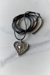 Collar con tiento encerado negro y dije dorado con forma de corazón texturizado.