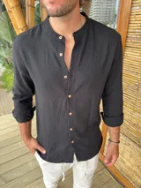 Camisa negra de corte slim, con cuello mao, manga larga con puños abotonados y cierre frontal con botones de madera.