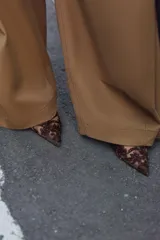 Zapato de tacón alto, destalonado, con punta fina. El cuerpo del zapato es de malla (mesh) color marrón oscuro, con apliques bordados y brillos en tonos similares. Posee una tira trasera elástica para ajuste.