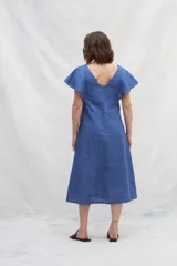 Vestido midi azul de lino con escote en V, mangas cortas con volados, bolsillos laterales y corte amplio. Presenta cintas verticales a contratono en el frente.