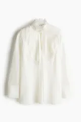 Blusa blanca de corte holgado en tejido transparente de mezcla de lyocell. Modelo de manga larga con cuello elevado de encaje, puños anchos abotonados y bajo recto. Pechera con abertura, alforzas y tiras spaghetti.