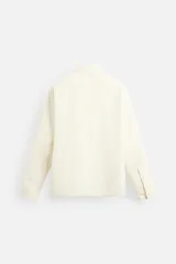 Sobrecamisa color crema de tejido técnico ligero, corte regular fit, cuello solapa, manga larga con puños abotonados, bajo ajustable con elástico en laterales y cierre frontal con cremallera.