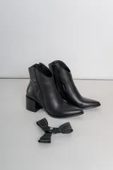 Bota corta de cuero color bordó, con taco cuadrado y punta fina. Presenta una correa con tachas pequeñas y una argolla metálica decorativa alrededor del tobillo. Cuenta con cierre lateral.