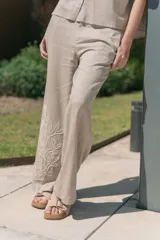 Conjunto de camisa de manga corta con cuello y pantalón de corte recto, ambos de tela simil lino color beige con bordados blancos.