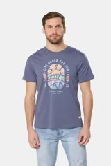 Remera blanca de manga corta con cuello redondo y un estampado gráfico frontal que simula un paisaje costero con un sol naciente o poniente, rodeado por texto circular que dice "SURF - LIFE UNDER THE SUN - CLUB".