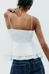 Top blanco de escote corazón y tirantes finos. Tiene corte peplum y cierre lateral con cremallera oculta.