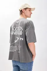 Camiseta manga corta gris oscuro con estampa de un paisaje marino y texto en color blanco. Corte amplio y recto, con proporciones cuadradas.