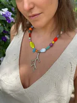 Collar corto con cuentas de cristal checo, cerámica y piedras reconstituidas de colores. Incluye separadores de acero quirúrgico y un dije plateado en forma de coral. Se cierra con cadena de acero quirúrgico para regular el largo.