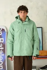 Chaqueta técnica color verde menta, con capucha ajustable, cierre frontal y múltiples bolsillos con cremallera. Presenta puños ajustables y un corte amplio, ideal para actividades al aire libre o deportes de invierno.