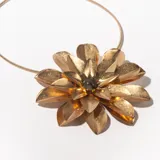 Collar dorado con dije grande en forma de flor con pétalos facetados y centro con cuentas negras. El collar es rígido y tiene una cadena extensible con cierre de mosquetón.