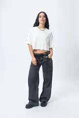 Remera blanca cropped de mangas cortas amplias con ojales metálicos a lo largo de las mangas.