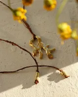 Collar con dije de bronce macizo de forma orgánica e irregular, color dorado, colgado de un cordón de seda natural marrón. El cordón tiene terminales cilíndricos dorados anudados.