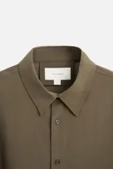 Camisa negra relaxed fit confeccionada en tejido fluido con mezcla de viscosa. Tiene cuello solapa, manga larga con puño abotonado y cierre frontal con botones.