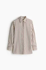 Camisa de crepé color crema con rayas verticales marrones, corte oversized, cuello clásico, cierre frontal con botones ocultos, mangas largas con puños abotonados, pliegue de caja invertido en la espalda y bajo recto.