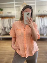 Camisa de lino y algodón color crudo, de corte recto, manga corta y cuello redondo con abertura frontal con botones. Tiene un bolsillo en el pecho con detalle de puntilla.