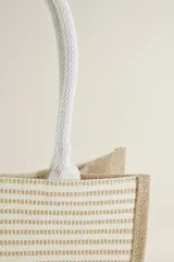 Bolso tipo tote de yute con rayas horizontales color beige y manijas de soga blanca.