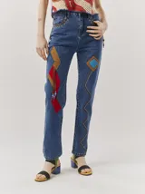Pantalón de jean azul con parches de colores, tiro alto, corte mom-fit, apliques de cuero trenzado alrededor de los bolsillos frontales y canutillos en la parte frontal.