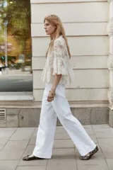 Pantalón de jean blanco, tiro alto, con pierna amplia y corte holgado. Presenta pliegues frontales y cierre de dos botones dorados.