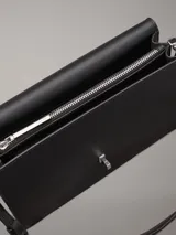 Cartera de hombro negra de cuero sintético con correa ajustable y cierre giratorio. Incluye bolsillo exterior trasero y compartimentos interiores con cremallera.