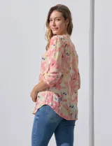 Blusa de gasa estampada con flores en tonos rosa, amarillo y azul. Tiene cuello a la base con escote en V y botones. La parte delantera tiene detalle plisado y las mangas son 3/4 regulables con presilla y botón.