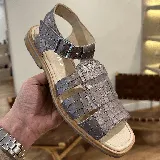 Sandalias de cuero color gris con textura tipo piel de cocodrilo, con hebilla metálica plateada y suela plana.