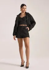 Chaqueta corta de tweed negro con detalles en blanco, cierre frontal con cremallera dorada y cuello clásico.