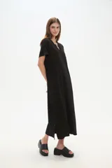 Vestido largo negro de manga corta, corte recto y holgado, con escote en V y un detalle de adorno tipo broche en el centro del escote.