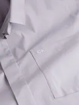 Camisa de manga corta color gris claro, corte boxy, cuello en punta, bolsillo de parche en el pecho y logo monograma de Calvin Klein estampado.