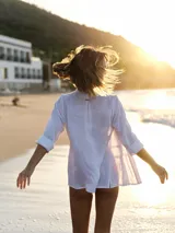 Camisa negra de lino con corte femenino, cuello clásico, cierre frontal con botones y mangas 3/4 con puños enrollados. Presenta detalles de frunces verticales en el frente y bolsillos de parche a la altura de la cadera.