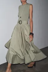 Vestido midi color verde oliva, de cuello redondo y sin mangas. Presenta un cinturón con hebilla metálica y detalle de volantes en la falda.