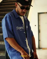 Camisa azul con rayas verticales blancas, de manga corta, cuello solapa y cierre frontal con botones. Estampado con el logo de la marca en el pecho.